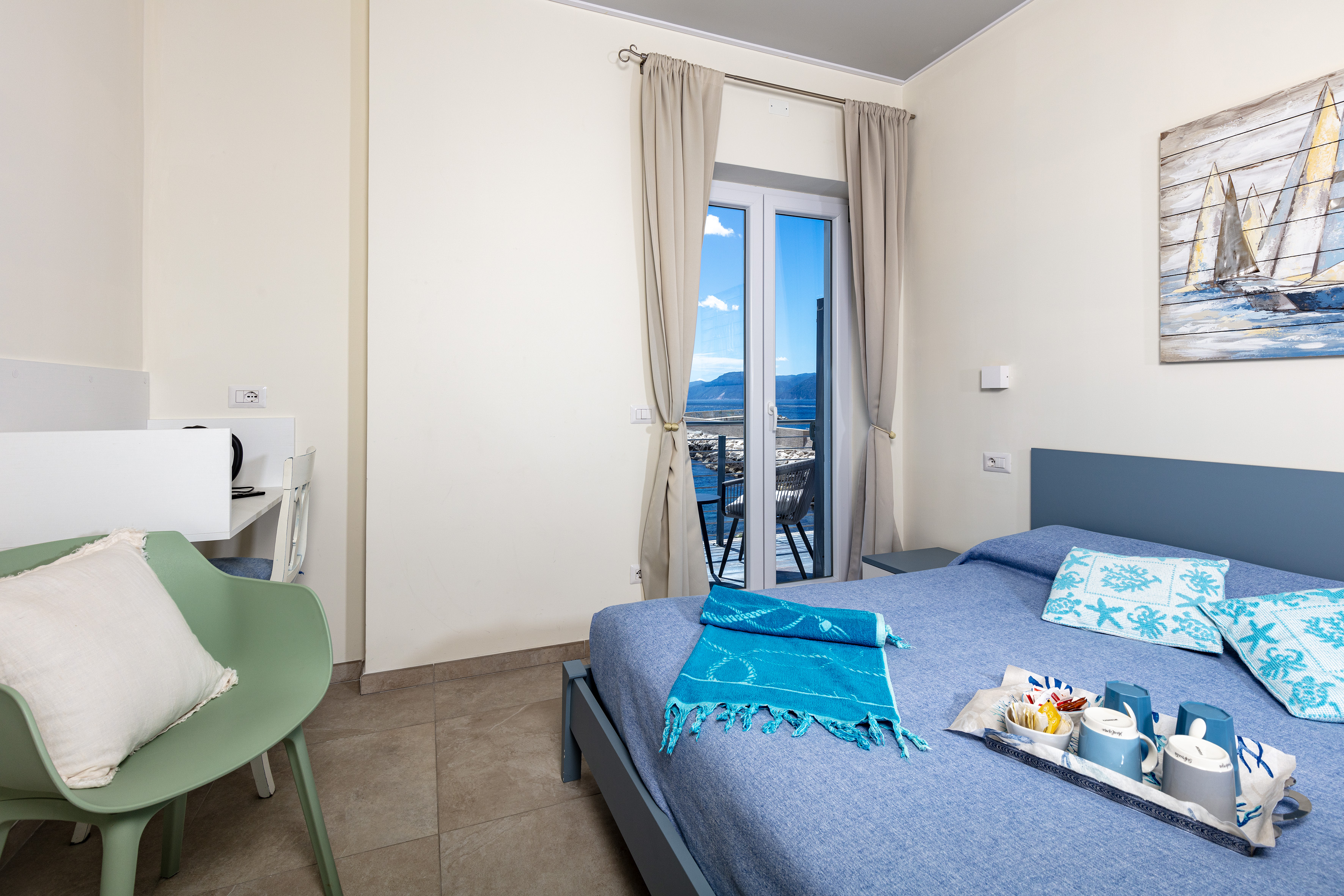 Camera della Casa del Pescatore con letto blu, telo turchese, vassoio colazione e portafinestra aperta sul mare